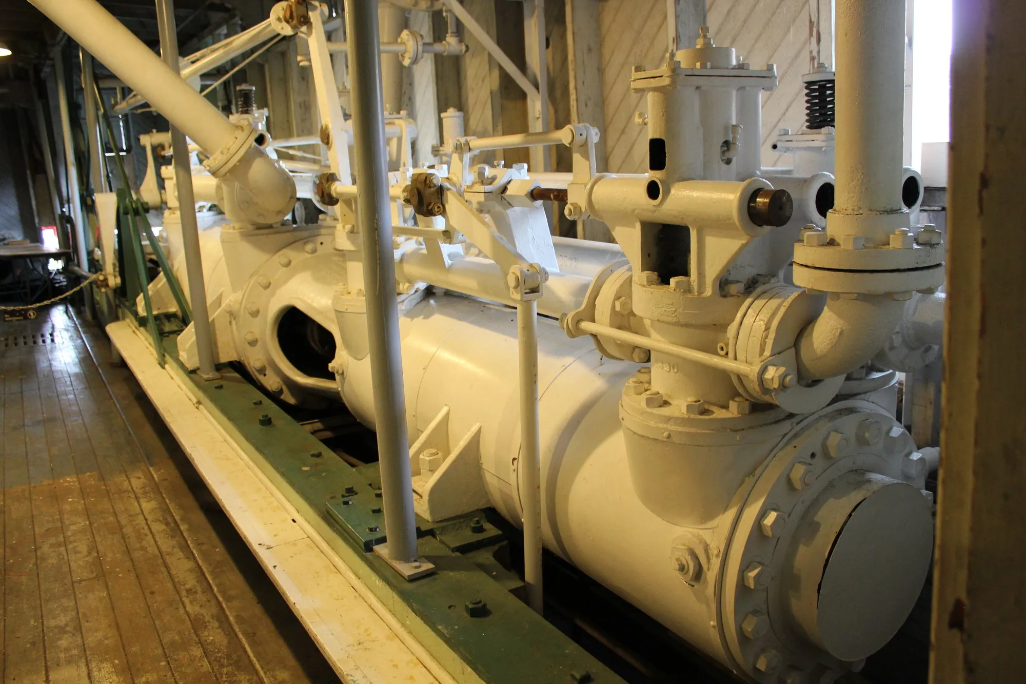 Long horizontal engine cylinder painted cream, with valve chest and steam pipe, on a timber bed
