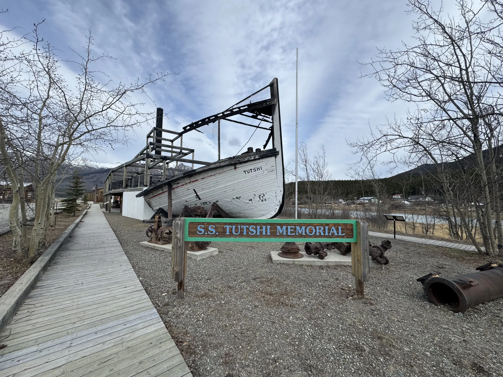 The SS Tutshi Memorial at Carcross, a white hull section and open steel frame outlining the upper decks, with a boardwalk and sign in front